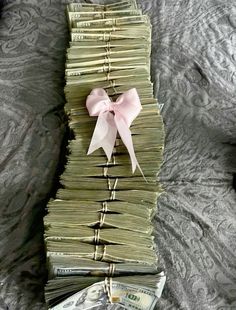 a stack of money sitting on top of a bed next to a pink bow tie