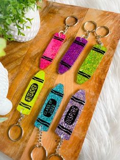 four glitter skateboard keychains sitting on top of a wooden board next to a plant