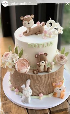 a three tiered cake with teddy bears and flowers on the top, sitting on a wooden table