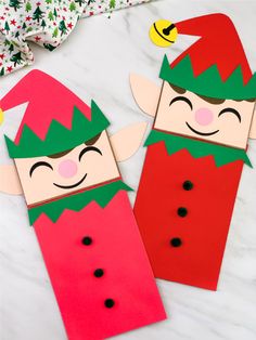 two paper cut out elfs sitting next to each other on a white marble surface