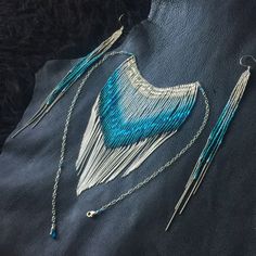 two pieces of jewelry are laying on a piece of black leather with beads and chains attached to it