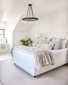 a bedroom with white walls and a chandelier hanging from the ceiling above the bed