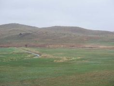 an open field with hills in the background and a stream running through the grass on either side