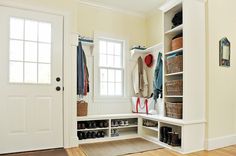 a white entryway with lots of shoes and baskets on the shelves next to it