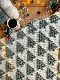 a crocheted christmas tree afghan next to a cup of coffee on a table