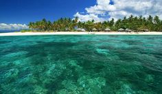 an island in the middle of water with palm trees on it's sides and blue skies above