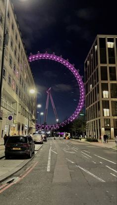 the london eye is lit up in purple for the night time celebration, as well as cars parked on the side of the road