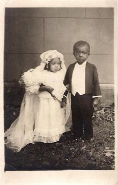 an old black and white photo of two children dressed in formal wear, standing next to each other