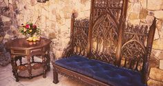 an ornate bench and table in front of a stone wall with flowers on it, next to a blue velvet cushion