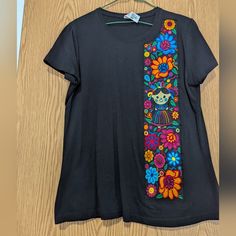 a black t - shirt with colorful flowers on it hanging from a wooden hanger