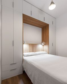 a white bed sitting in a bedroom next to a wooden headboard and cupboards