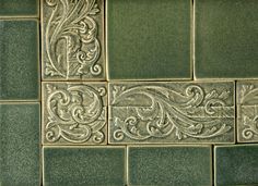 a green tile wall with decorative designs on it