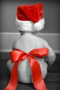 a black and white photo of a baby wearing a santa hat sitting on the floor