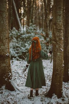 a woman with long red hair standing in the snow between two trees, looking at something