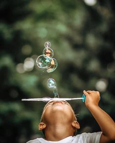 a young boy blowing bubbles on top of a stick with an object in the air above his head