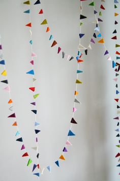 multicolored paper garland hanging from the ceiling in front of a white wall with two vases on it