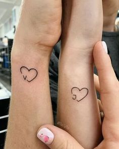 two people with matching tattoos on their arms holding each other's hands and looking at the camera