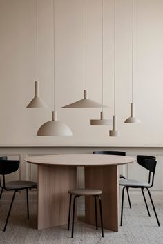 a dining room table with four chairs and three pendant lights hanging from the ceiling above it