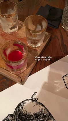 two glasses with red liquid sit on a wooden tray