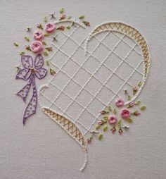 an embroidered heart with pink flowers and ribbons on it's side, sitting on a white piece of cloth