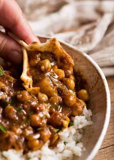 a hand holding a spoon over some rice and beans in a bowl on a wooden table