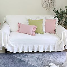 a white couch with pink and green pillows in a living room next to a potted plant