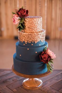 a three tiered blue and gold wedding cake on a wooden table with pink flowers