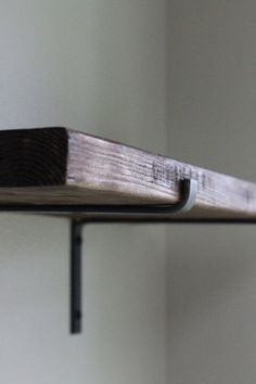 a wooden shelf sitting on top of a white wall next to a black metal pipe