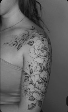 a woman's shoulder with flowers and leaves tattooed on her left arm, in black and white