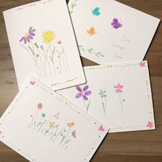 four cards with flowers on them sitting on top of a wooden table next to each other