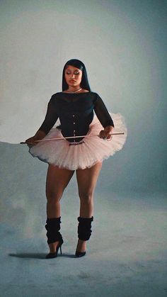 a woman in a black shirt and pink tutu skirt holding a white object with one hand