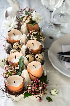 an arrangement of decorated eggs and flowers on a dining room table with place settings in the background