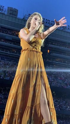 a woman in a yellow dress on stage with her hands out to the side,