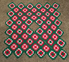 a green and red crocheted tablecloth with white flowers in the center on a carpeted floor