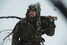 a man in winter clothes carrying a large tree branch with snow falling all over him