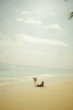 a person laying on the beach with their feet in the sand under a palm tree