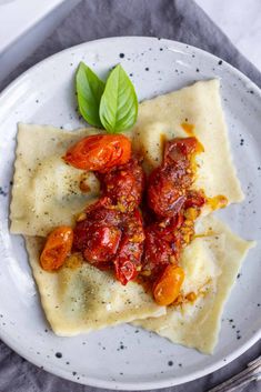 two ravioli with tomatoes and basil on a white plate