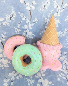 two doughnuts and an ice cream cone are sitting on a blue floral background