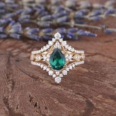 an emerald and diamond ring sitting on top of a wooden table next to lavender flowers