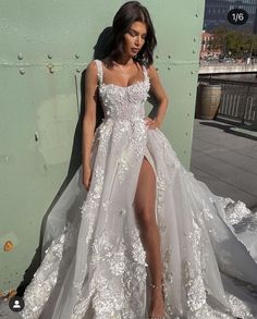 a woman in a white wedding dress leaning against a wall with her leg on the ground