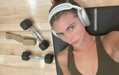 a woman with headphones laying on a mat next to dumbbells