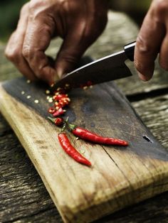 a person cutting up red peppers on top of a wooden cutting board