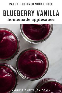 four jars filled with blueberry vanilla homemade applesauce sitting on a marble counter top