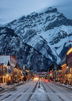 a snowy mountain is in the distance with buildings on both sides and street lights lit up at night