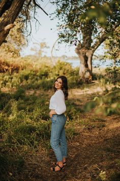 a woman standing in the woods with her hands on her hips and looking up at the sky