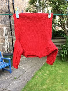 a red sweater hanging on a clothes line outside in the yard with two blue chairs next to it