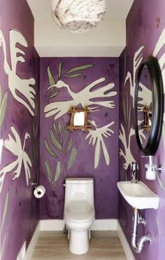 a bathroom decorated in purple and white with flowers painted on the walls, toilet and sink