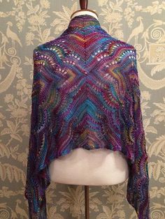 a knitted shawl on top of a mannequin head in front of a wallpapered background