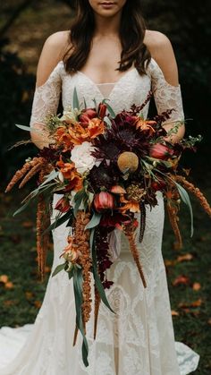 a woman in a wedding dress holding a bouquet with flowers and foliage on the side