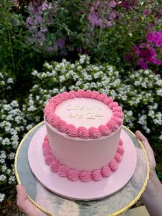 a pink cake sitting on top of a white plate in front of purple and white flowers